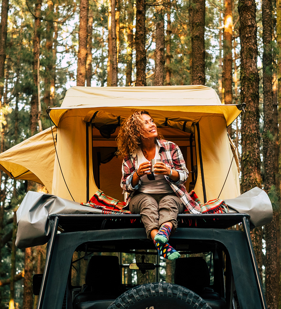 A woman sitting on top of a jeep in the woods, feeling a migraine.